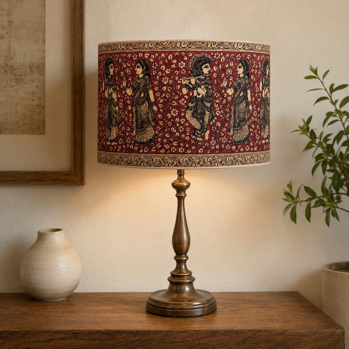 Varnya Kalamkari-print cotton drum lampshade in deep red on a brass table lamp beside a warm cream wall